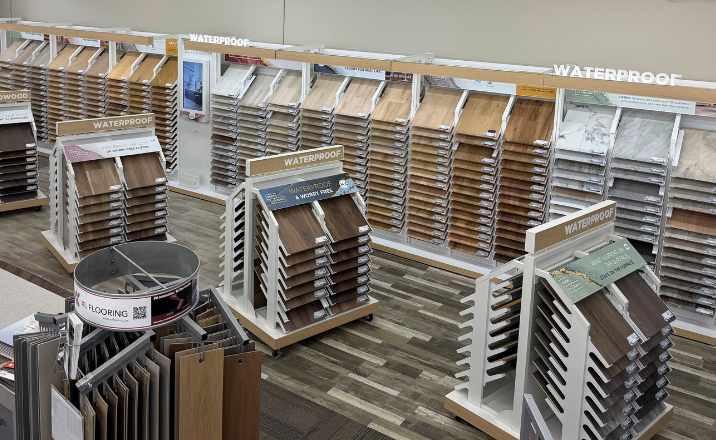Swift Current Carpet One showroom display featuring numerous samples of wood and stone-look flooring options organized on tiered racks.